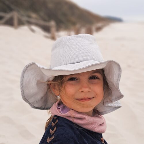 bawełniany kapelusz na lato i uśmiechnięta dziewczynka siedząca na plaży